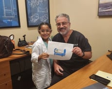 Dr. Katz and little girl in doctor coat holding up hand drawn picture